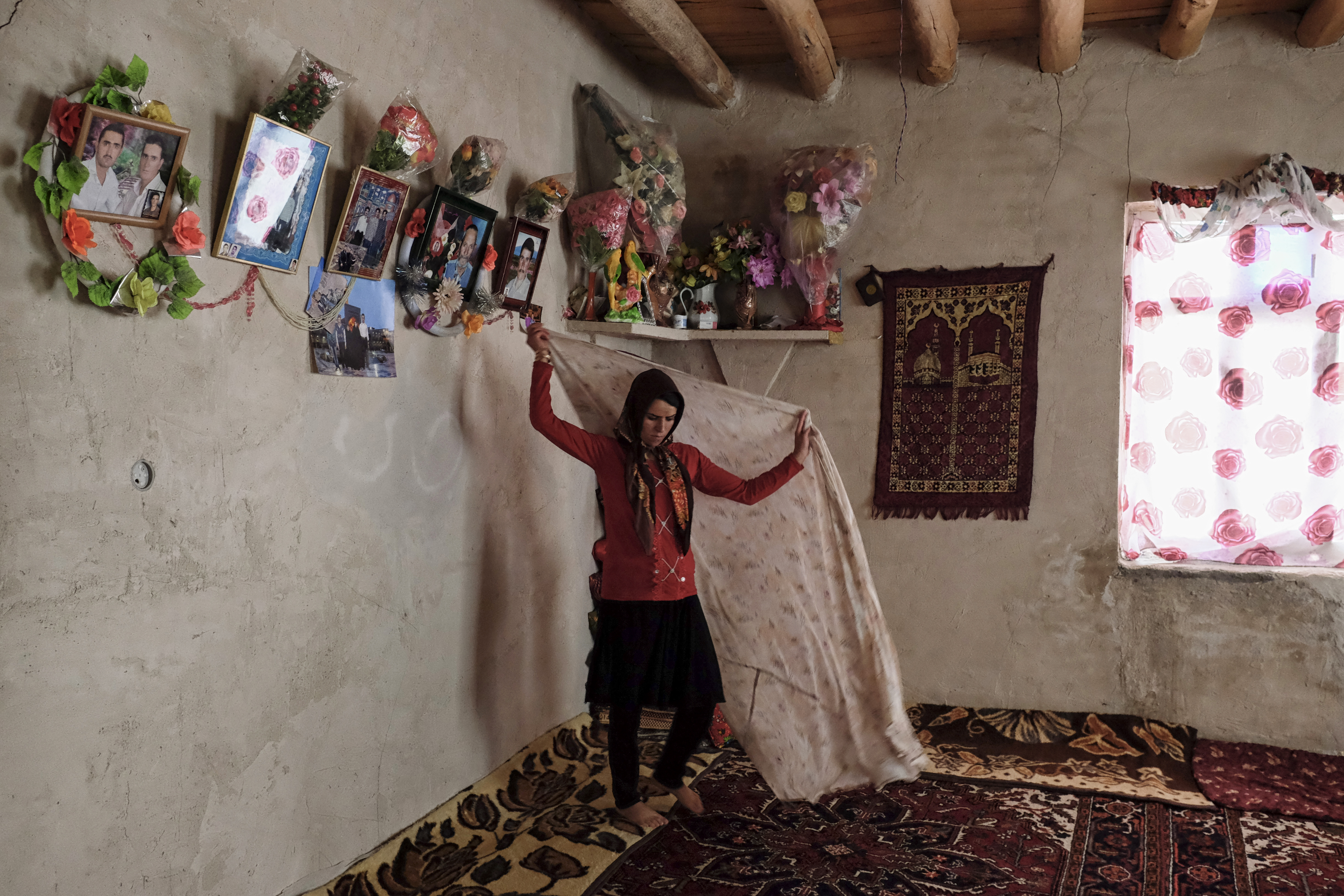 Roghayyeh in the room where she usually sleeps, stands alone below family photos. Ajabshir, East Azerbaijan, Iran.